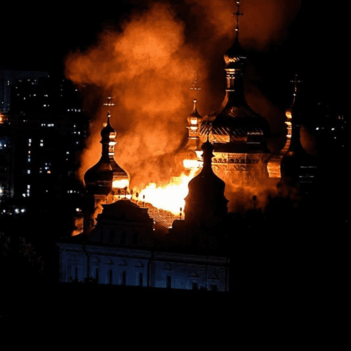 Kyiv-Pechersk Lavra burns at night, with bright flames engulfing part of the historic church complex as thick orange smoke rises behind its dark domes.